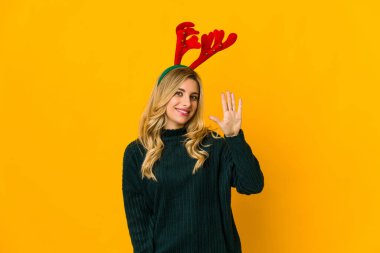 Ren geyiği boynuzu takan genç sarışın kadın gülümseyerek beş numarayı parmaklarıyla gösteriyor..