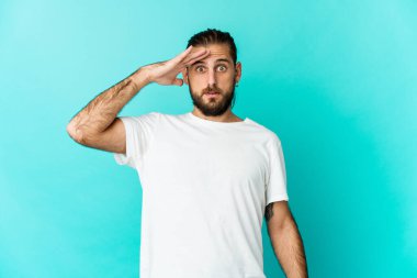 Uzun saçlı genç adam yüksek sesle bağırıyor, gözleri açık ve elleri gergin tutuyor..