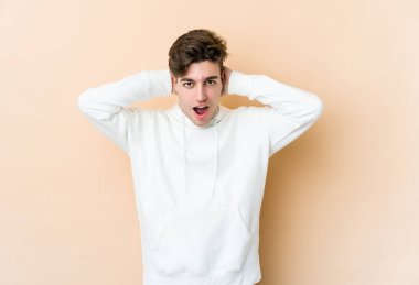 Beyaz tenli genç adam bej arka planda izole edilmiş bağırıyor, çok heyecanlı, tutkulu, bir şeyden memnun..