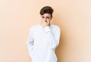 Beyazlı genç bir adam bej arka planda izole edilmiş ağzı kapalı ve elleri endişeli görünüyor..