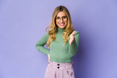 Beyaz tenli sarışın kadın selamlama jesti olarak kameraya elini uzatıyor..