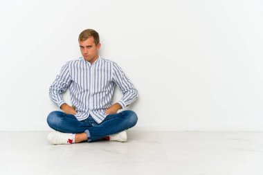 Kafkasyalı genç adam yerde oturuyor hoşnutsuzca kaşlarını çatıyor, kollarını kavuşturuyor..