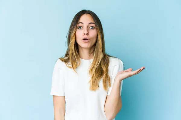 Jovem Mulher Caucasiana Isolado Fundo Azul Impressionado Segurando Espaço Cópia — Fotografia de Stock