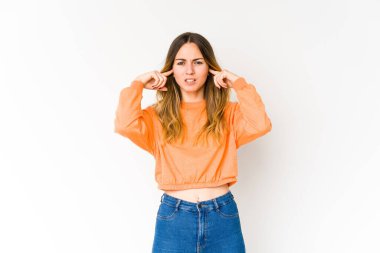 Beyaz arka planda izole edilmiş genç beyaz bir kadın parmaklarıyla kulaklarını kapatıyor, gürültülü bir ortam yüzünden stresli ve çaresiz..