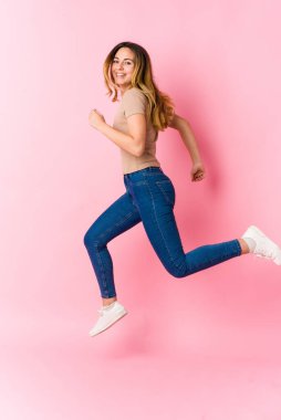 Pembe arka planda atlayan beyaz, sarışın genç bir kadın.