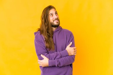 Uzun saçlı genç adam kollarını kavuşturarak gülümsüyor..