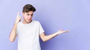 Mor arka planda izole edilmiş genç beyaz adam elinde bir ürün tutuyor..