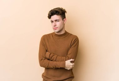 Beyazlı genç bir adam bej arka planda izole edilmiş şüpheli, belirsiz, seni muayene ediyor..