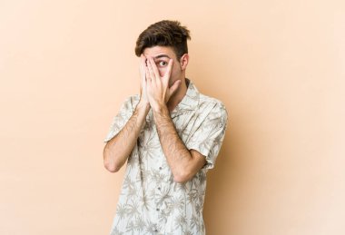 Beyazlı genç bir adam bej arka planda izole edilmiş. Korkmuş ve gergin parmaklarıyla göz kırp..