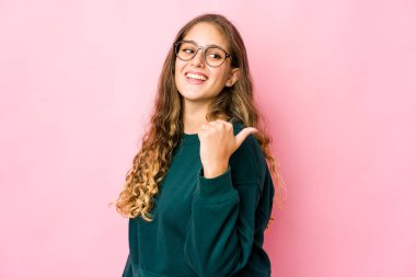 Genç beyaz kadın başparmağıyla işaret ediyor, gülüyor ve kaygısız..