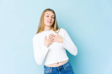 Mavi arka planda izole edilmiş genç sarışın kadın dost canlısı bir ifadeye sahip, avuçlarını göğsüne bastırıyor. Aşk konsepti.