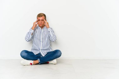 Genç, beyaz bir adam yerde oturmuş şakaklara dokunuyor ve başı ağrıyor..