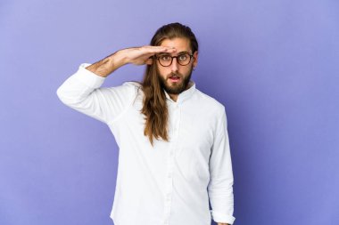 Uzun saçlı genç adam yüksek sesle bağırıyor, gözleri açık ve elleri gergin tutuyor..