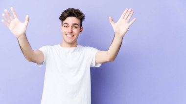 Mor arka planda izole olmuş genç beyaz bir adam zaferi ya da başarıyı kutluyor, şaşırıyor ve şok oluyor..