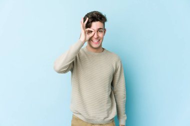 Kafkasyalı genç adam mavi arka planda izole edildi. Heyecanlı görünüyor..