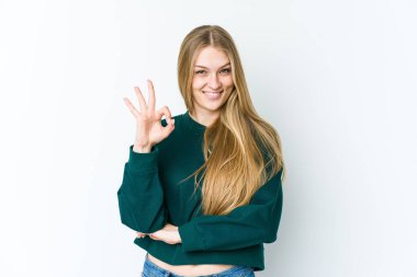 Beyaz arka planda izole edilmiş genç sarışın bir kadın bir göz kırptı ve elleriyle iyi bir jest yaptı..