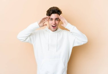 Beyaz tenli genç adam bej arka planda izole edilmiş. Hoş bir sürpriz bekliyor. Heyecanlı ve el kaldırıyor..