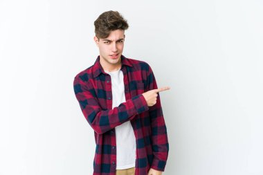 Beyaz arka planda izole edilmiş genç beyaz bir adam gülümsüyor ve boş alanda bir şeyler gösteriyor..