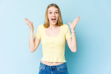 Mavi arka planda kalan genç sarışın kadın zaferi ya da başarıyı kutluyor, şaşırıyor ve şok oluyor..