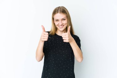 Beyaz arka planda izole edilmiş genç sarışın kadın gülümsüyor ve başparmağını kaldırıyor.
