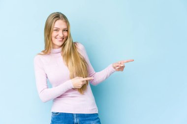 Mavi arka planda izole edilmiş genç sarışın kadın işaret parmağıyla işaret ettiği için heyecanlı..