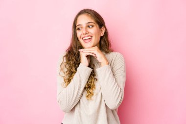 Genç beyaz kadın ellerini çenesinin altında tutuyor, mutlu bir şekilde yan tarafa bakıyor..