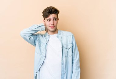 Kafkasyalı genç adam bej arka planda izole edilmiş kafasının arkasına dokunuyor, düşünüyor ve bir seçim yapıyor..