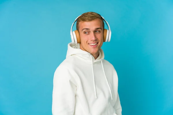 Mladý Kavkazský Muž Poslouchající Hudbu Izolovanou Modrém Pozadí Dívá Stranou — Stock fotografie