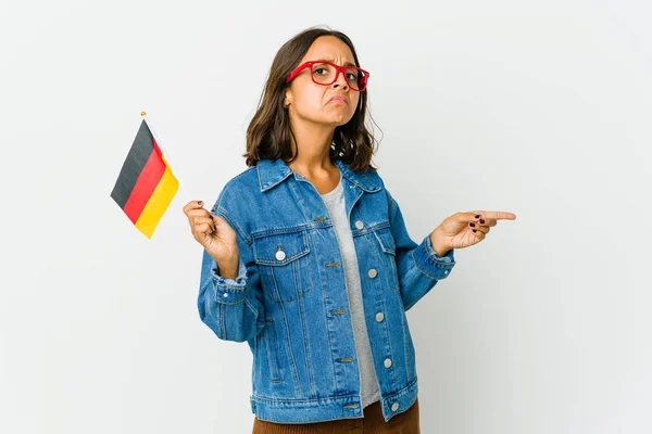 白い背景に隔離されたドイツの旗を持っている若いラテン語の女性は コピースペースにインデックス指で指してショックを受けました — ストック写真