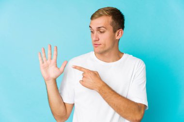 Genç beyaz yakışıklı adam gülümseyerek beş numarayı parmaklarıyla gösteriyor..
