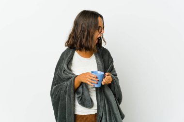 Beyaz arka planda battaniyeli genç Latin kadın çok kızgın, öfkeli, hayal kırıklığına uğramış.