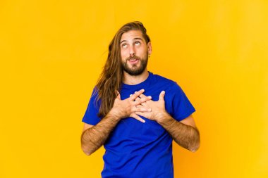 Uzun saçlı genç adam samimi bir ifadeye sahip, avuçlarını göğsüne bastırıyor. Aşk konsepti.