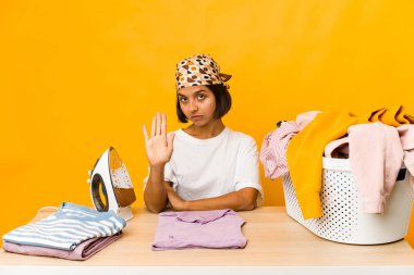 Elbiselerini ütüleyen genç İspanyol kadın elini uzatmış, dur işareti gösteriyor ve seni engelliyor..