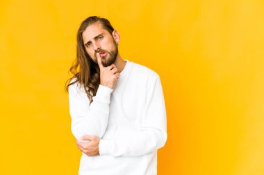 Uzun saçlı genç adam, iğneleyici ifadesiyle kameraya bakarken mutsuz görünüyor..