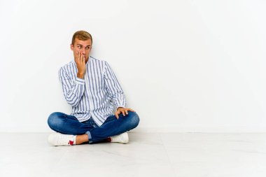 Genç beyaz adam yerde oturuyor ve bir şey yüzünden şoka uğruyor.