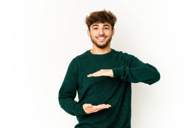 Beyaz arka plandaki genç Arap adam iki eliyle bir şey tutuyor, ürün sunumu..