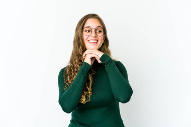 Genç beyaz kadın ellerini çenesinin altında tutuyor, mutlu bir şekilde yan tarafa bakıyor..