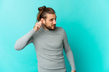 Uzun saçlı genç adam kulaklarını parmaklarıyla kapatıyor, stresli ve çaresiz, gürültülü bir ortam tarafından..