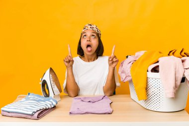 Giysileri ütüleyen genç İspanyol kadın üst tarafı açık ağızla işaret ediyor..