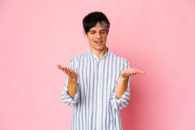 Young skinny hispanic man holding something with palms, offering to camera.