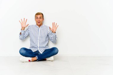 Genç beyaz adam yerde oturuyor. Hoş bir sürpriz bekliyor. Heyecanlı ve el kaldırıyor..