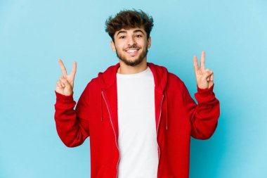 Mavi arka planda genç bir Arap zafer işareti gösteriyor ve gülümsüyor..