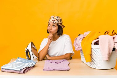 Giysilerini ütüleyen genç İspanyol kadın şüpheli ve şüpheci bir ifadeyle yana bakıyor..