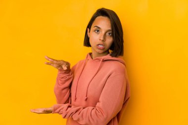 Sarı üzerine izole edilmiş genç İspanyol kadın elleri arasında bir kopya alanı tutarken şok olmuş ve hayrete düşmüş..