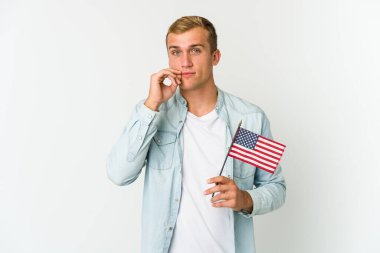 Beyaz arka planda izole edilmiş Amerikan bayrağı tutan genç beyaz bir adam. Parmakları dudaklarında bir sır saklıyor..