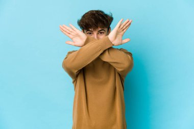 Mavi arka plandaki genç Arap adam iki kolu çapraz tutuyor, inkar kavramı.