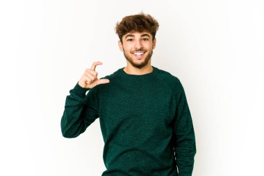 Beyaz arka plandaki genç Arap adam işaret parmaklarıyla küçük bir şey tutuyor, gülümsüyor ve kendinden emin..