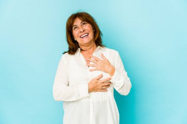 Beyaz kadın mutlu bir şekilde gülüyor ve ellerini karnının üstünde tutarak eğleniyor..