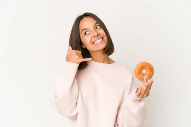 Donut yiyen genç İspanyol kadın cep telefonu hareketini parmaklarıyla gösteriyor..