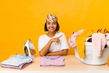 Elbiselerini ütüleyen genç İspanyol kadın. Gülümsüyor ve bir kenara işaret ediyor. Boş alanda bir şey gösteriyor..